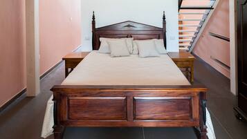 A bedroom with a large wooden bed, a nightstand, and a staircase in the background.