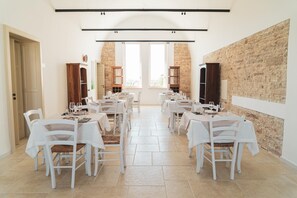 A dining area with white tables and chairs, a stone wall, and large windows.