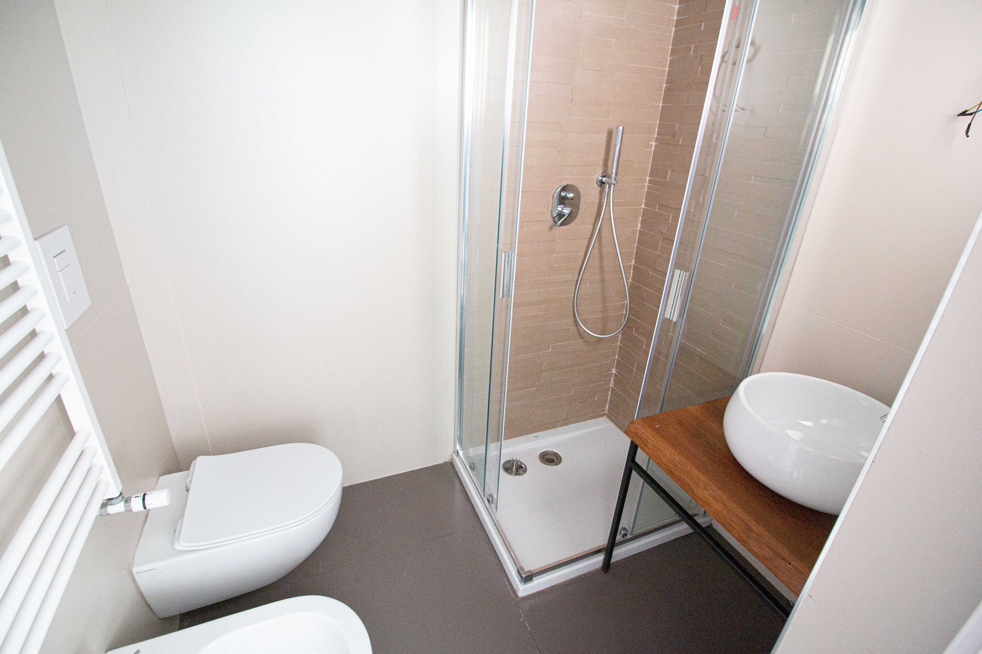A modern bathroom with a glass-enclosed shower, a white toilet, and a wooden vanity with a sink.