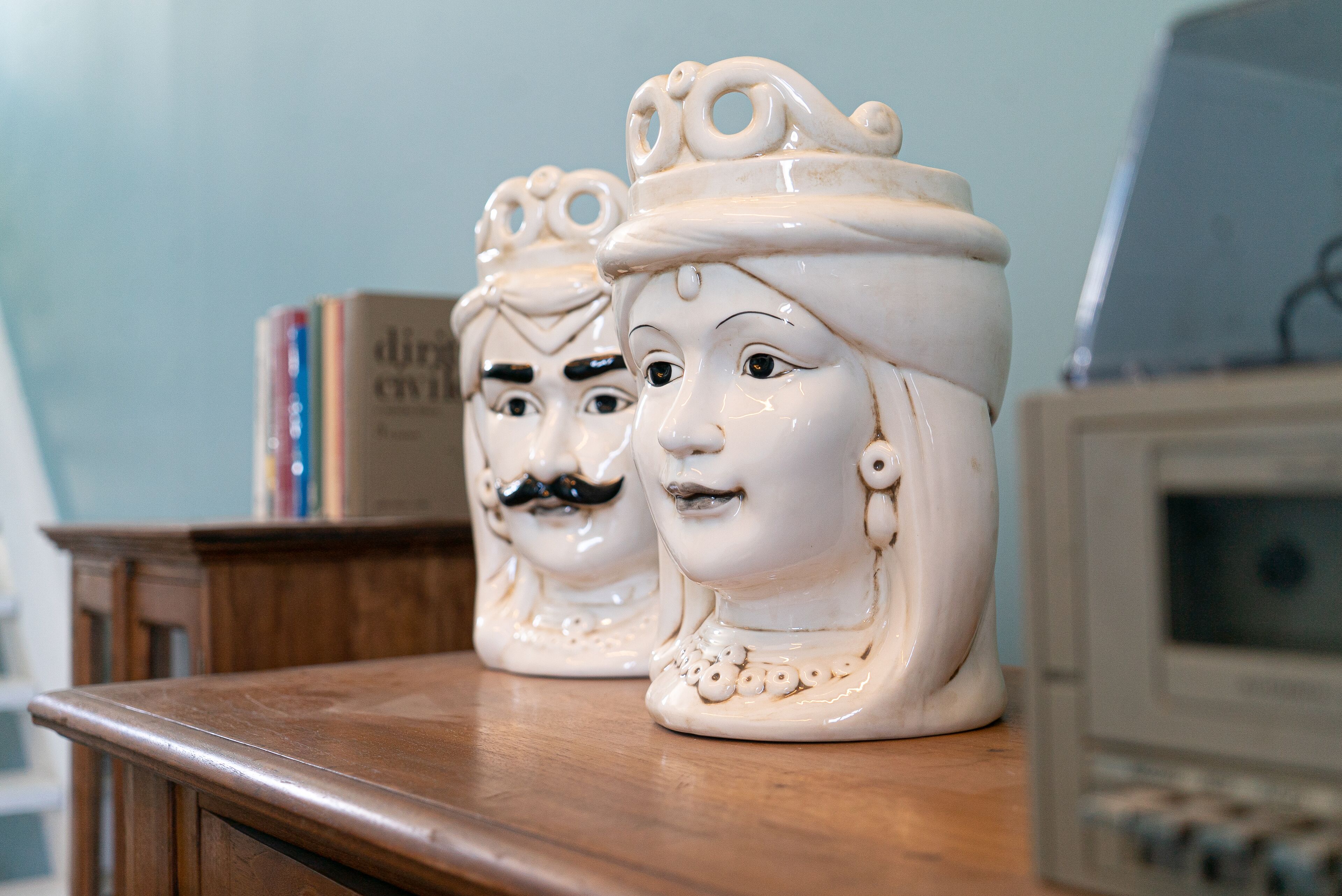 Two ceramic head vases on a wooden surface with a bookshelf and an old television in the background.