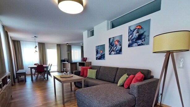 A modern living room with a grey sofa, a dining table, and a lamp. There are three abstract paintings on the wall. - Whg.5 Ferienwohnung Landglück (Bechhofen)