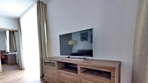 A modern living room with a flat-screen TV on a wooden console, a dining area with a table and chairs, and a large window with curtains. - Whg.5 Ferienwohnung Landglück (Bechhofen)