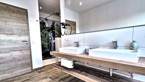 Ein modernes Badezimmer mit Holzboden, zwei Waschbecken, einem großen Spiegel und einer Dusche mit Blick auf einen Wasserfall.