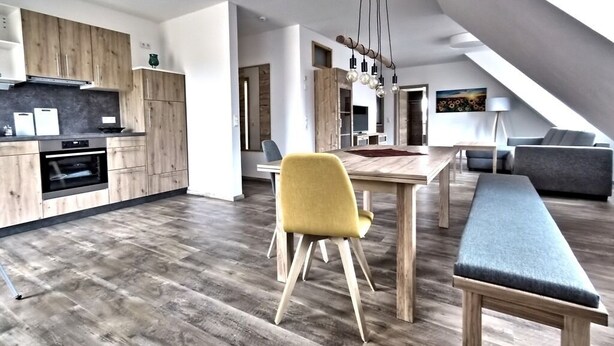 Eine moderne Küche mit Holzausbau, ein Essbereich mit einer Bank und ein Wohnbereich im Loft-Stil mit einer Couch.
