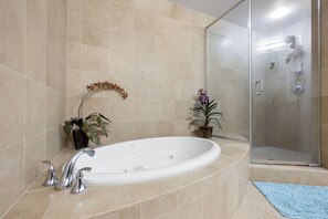 A bathroom with a bathtub, a glass shower enclosure, and two potted plants.