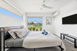 Quarto com cama, ventoinha no teto, janela com vista, televisão de tela plana e um banco.