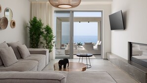 Un salon moderne avec un canapé, une table basse et une petite figurine d’éléphant. Une grande fenêtre offre une vue sur l’océan.