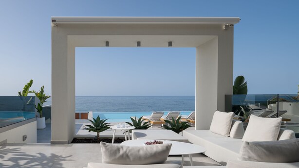 Un espace de détente extérieur moderne avec vue sur l’océan, comprenant des meubles blancs, une balustrade en verre et des plantes en pot.