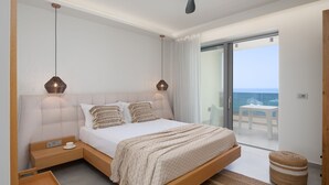 Une chambre à coucher comprenant un lit, des tables de chevet, un ventilateur de plafond et une vue sur l’océan, accessible par une porte-fenêtre coulissante.
