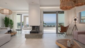 Un salon moderne doté d’une cheminée, de grandes fenêtres et offrant une vue sur l’océan.