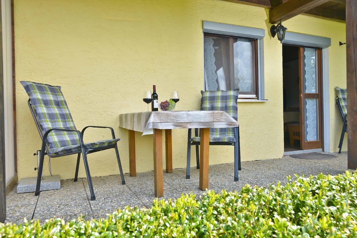 Ein Sitzbereich im Freien mit Tisch und Stühlen, einem Fenster und einer Tür.
