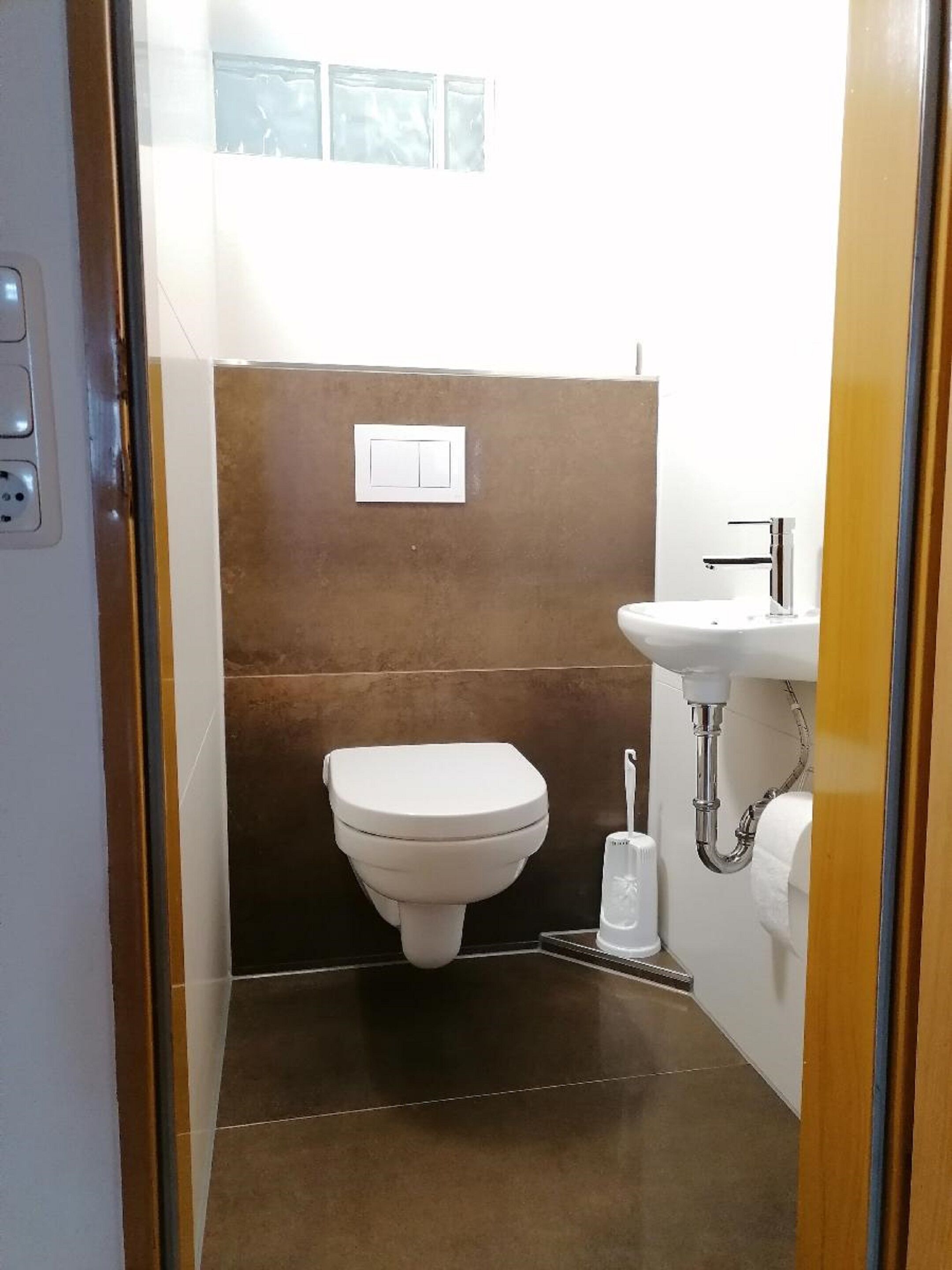 A compact bathroom with a white toilet, a sink with a chrome faucet, and a wall-mounted light switch.