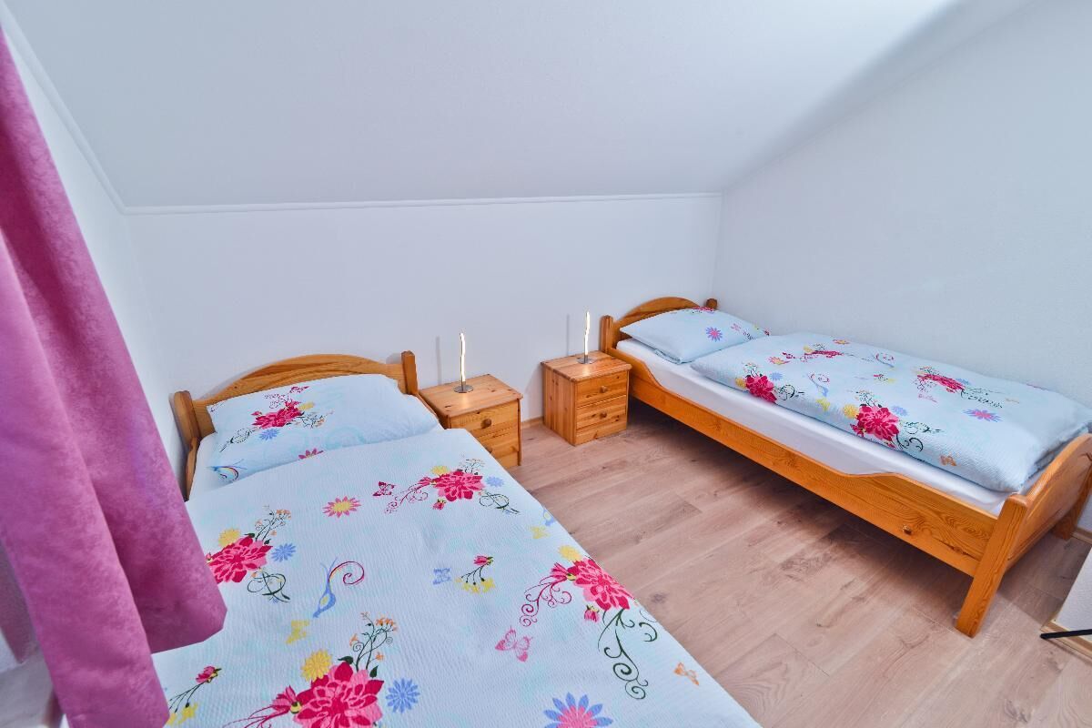 Une chambre avec deux lits simples, des têtes de lit en bois et une table de chevet sur laquelle est posée une bougie, entre les deux lits.