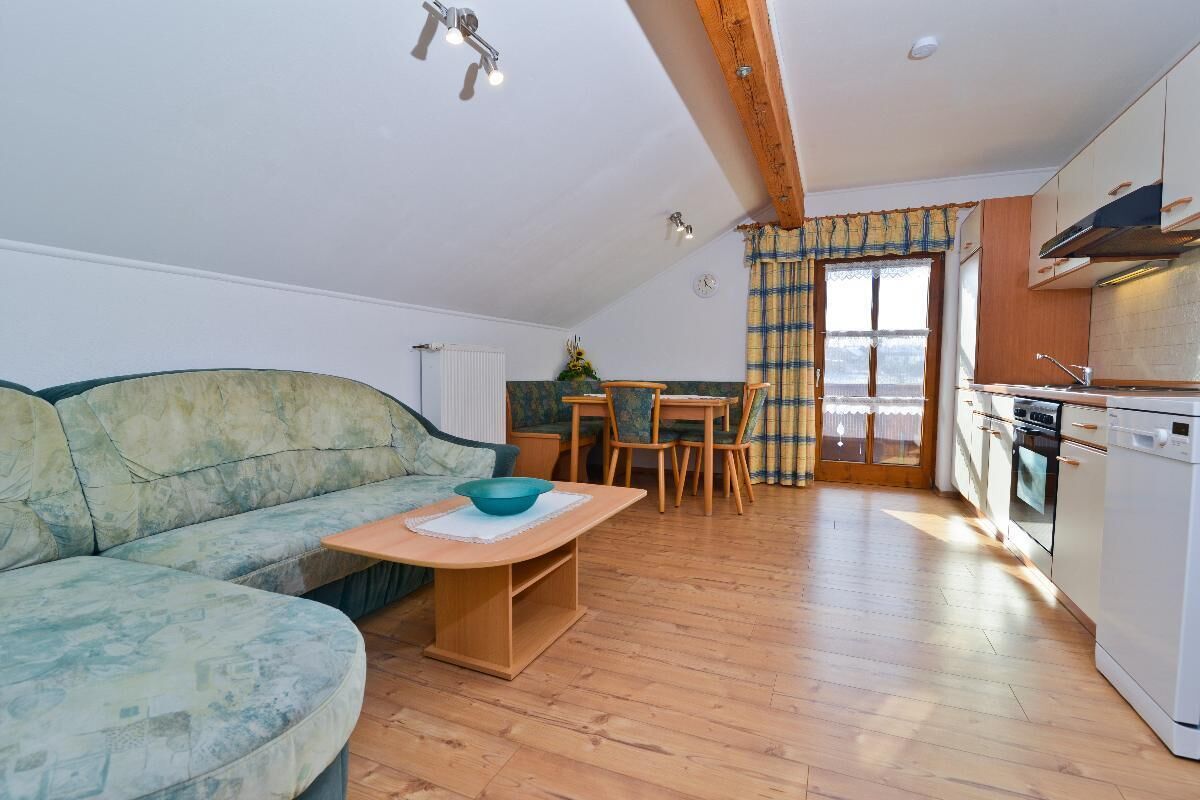 A cozy living room with a sofa, a wooden coffee table, and a dining area with a table and chairs. A kitchen with a stove and cabinets is visible in the background.