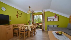 Een eetgedeelte met een tafel en stoelen, een televisie en een raam met gordijnen.