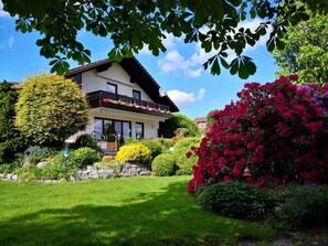A two-story house with a balcony, surrounded by well-maintained gardens and a clear blue sky. - Ferienwohnung Kreuzer Lydia (Furth im Wald)