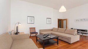 Uma sala de estar moderna com um sofá, uma mesa de centro e uma luminária. Há quadros nas paredes e uma porta que dá para outro cômodo.