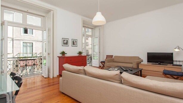 Uma sala de estar moderna com sofá, uma cômoda vermelha, televisão e uma varanda com vista para edifícios.