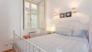 Quarto com cama, janela, radiador e luminárias fixadas na parede.