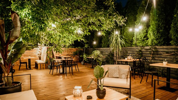 Un espace extérieur aménagé en terrasse, avec un sol en bois, des tables, des chaises et des plantes en pot.