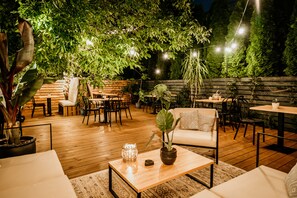 Un espace extérieur aménagé en terrasse, avec un sol en bois, des tables, des chaises et des plantes en pot.