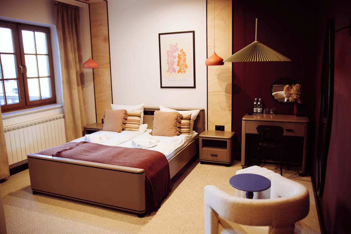Habitación de hotel con cama, mesita de noche, silla, escritorio y ventana con cortinas.