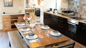 A modern kitchen with wooden beams, a long dining table set for six, and a built-in oven. - Charming house, quiet, in the heart of the Parc du Perche, 50m from the forest (CONDEAU)