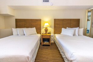 A hotel room with two beds, a nightstand with a lamp, and a wooden headboard. - Beach Colony 403 (Myrtle Beach)