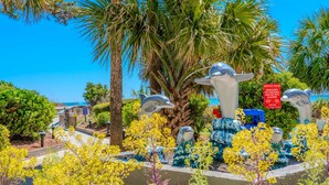 Un jardin agrémenté de sculptures de dauphins, de palmiers et surplombé d’un ciel d’un bleu limpide.