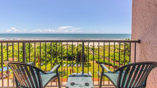 Un balcon avec vue sur la plage, deux chaises et une table.