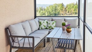 Un balcon doté d’un espace salon avec des coussins, d’une petite table et offrant une vue sur les arbres et les collines.