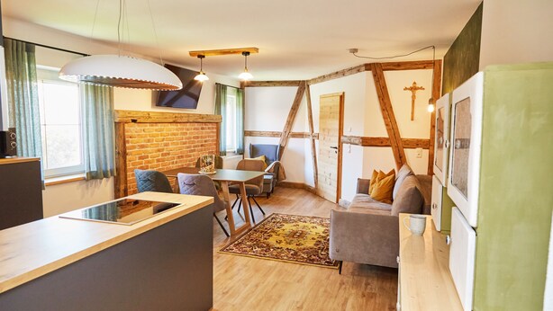 Une cuisine moderne dotée d’un îlot central, un coin repas avec une table et des chaises, et un espace salon confortable avec un canapé et des coussins.