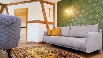 A room with a grey sofa, a patterned rug, wooden beams, and a green wall with a leaf design.