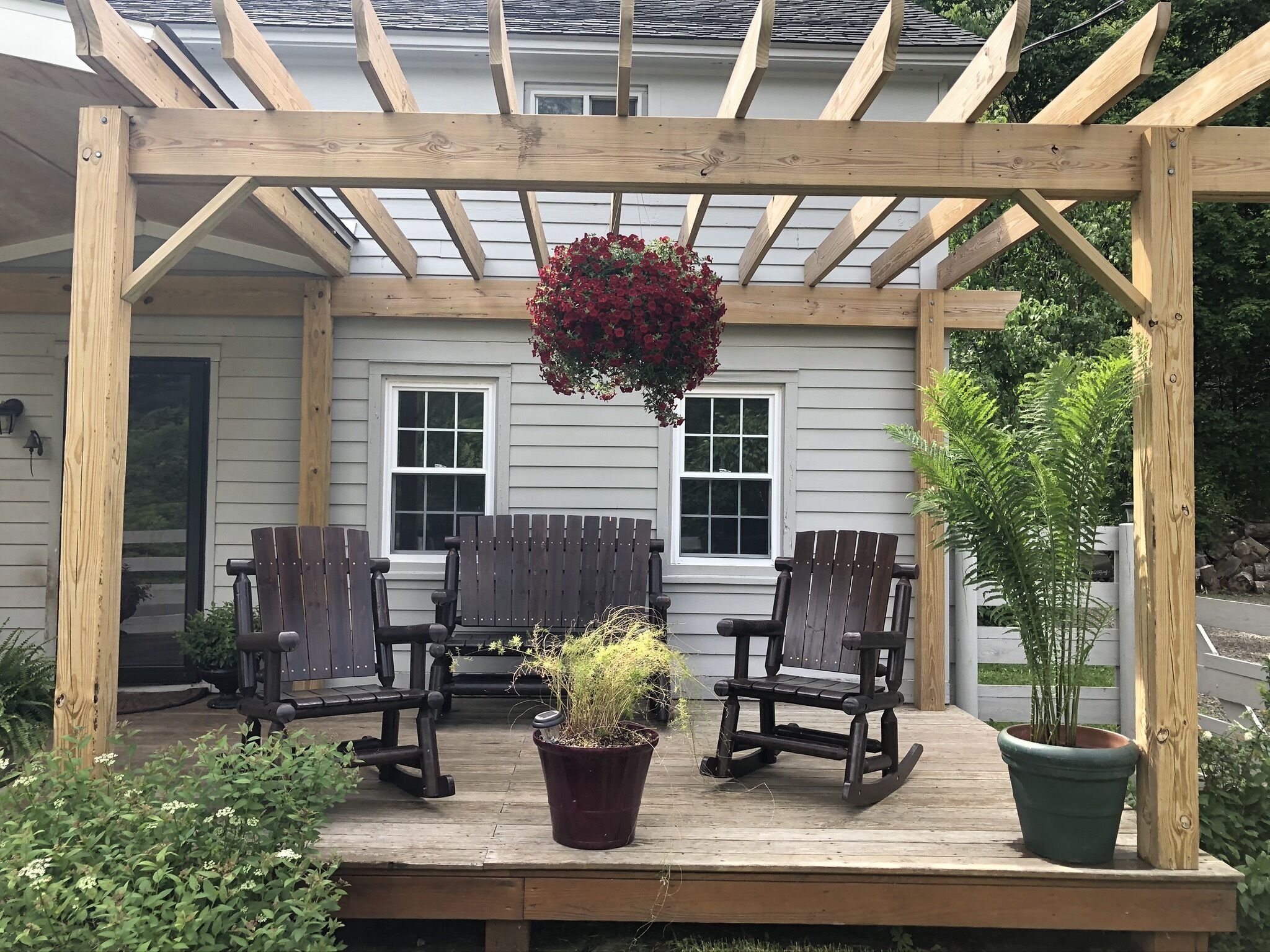 A wooden deck with two rocking chairs and a hanging flower basket.