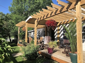 A wooden pergola with hanging flower baskets, outdoor seating, and potted plants.