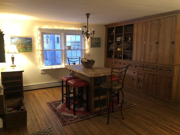 A cozy kitchen with a wooden island, red bar stools, a chandelier, and a large wooden cabinet with glass doors.