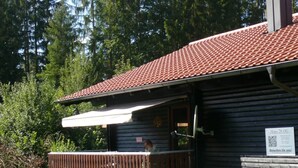A wooden cabin with a tiled roof, a balcony, and a sign with a QR code.