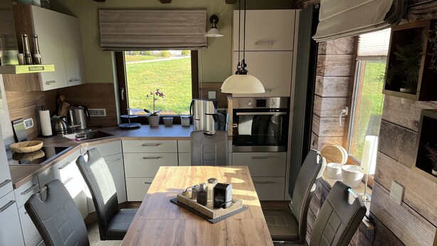 A modern kitchen with a wooden table, built-in appliances, and a view of the outdoors.