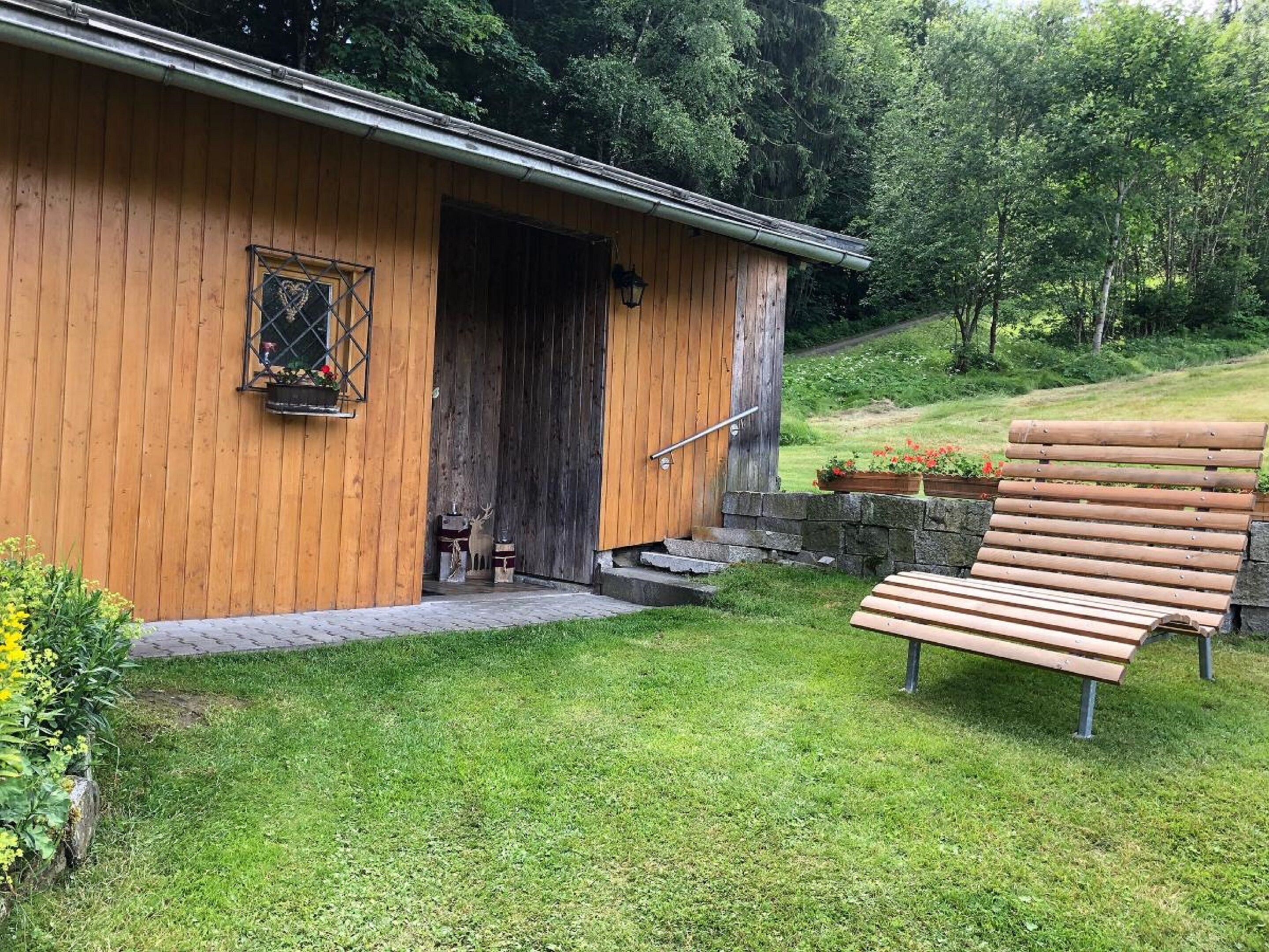 A wooden cabin with a wooden door, a bench, and a stone wall.