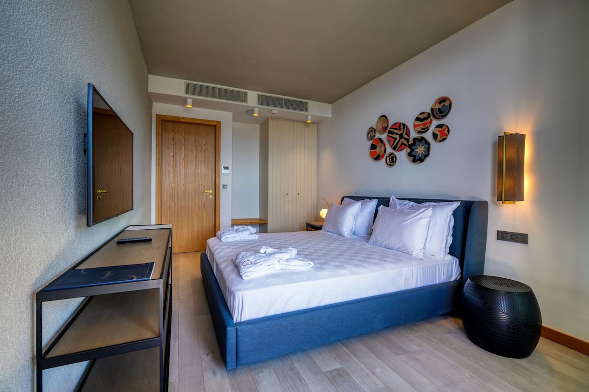 A modern hotel room with a large bed, a desk, a TV, and a wall with decorative plates.