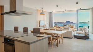 Une cuisine moderne dotée d’un grand îlot central, d’un coin repas avec des chaises et d’un espace détente offrant une vue sur l’océan.