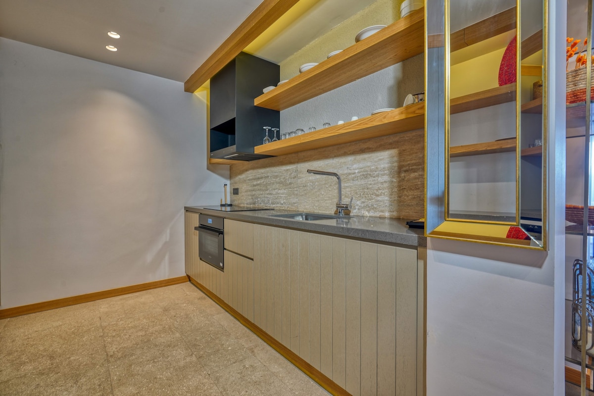 A compact kitchen with a built-in oven, a sink, and wooden shelves above the countertop.