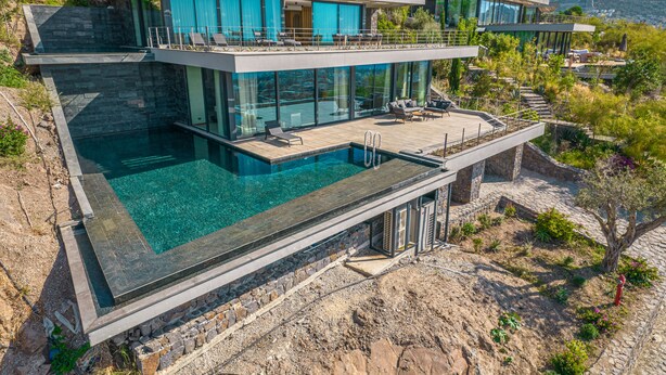 Une maison moderne à deux étages, dotée d’une grande piscine à débordement et d’un espace salon extérieur.