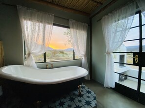 A bathroom with a freestanding bathtub, a window with curtains, and a view of the landscape.
