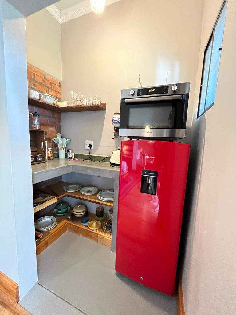 Une cuisine de taille réduite avec un réfrigérateur rouge, un four à micro-ondes et un mur de briques derrière l’évier.