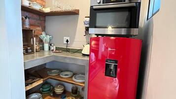 Une cuisine de taille réduite avec un réfrigérateur rouge, un four à micro-ondes et un mur de briques derrière l’évier.