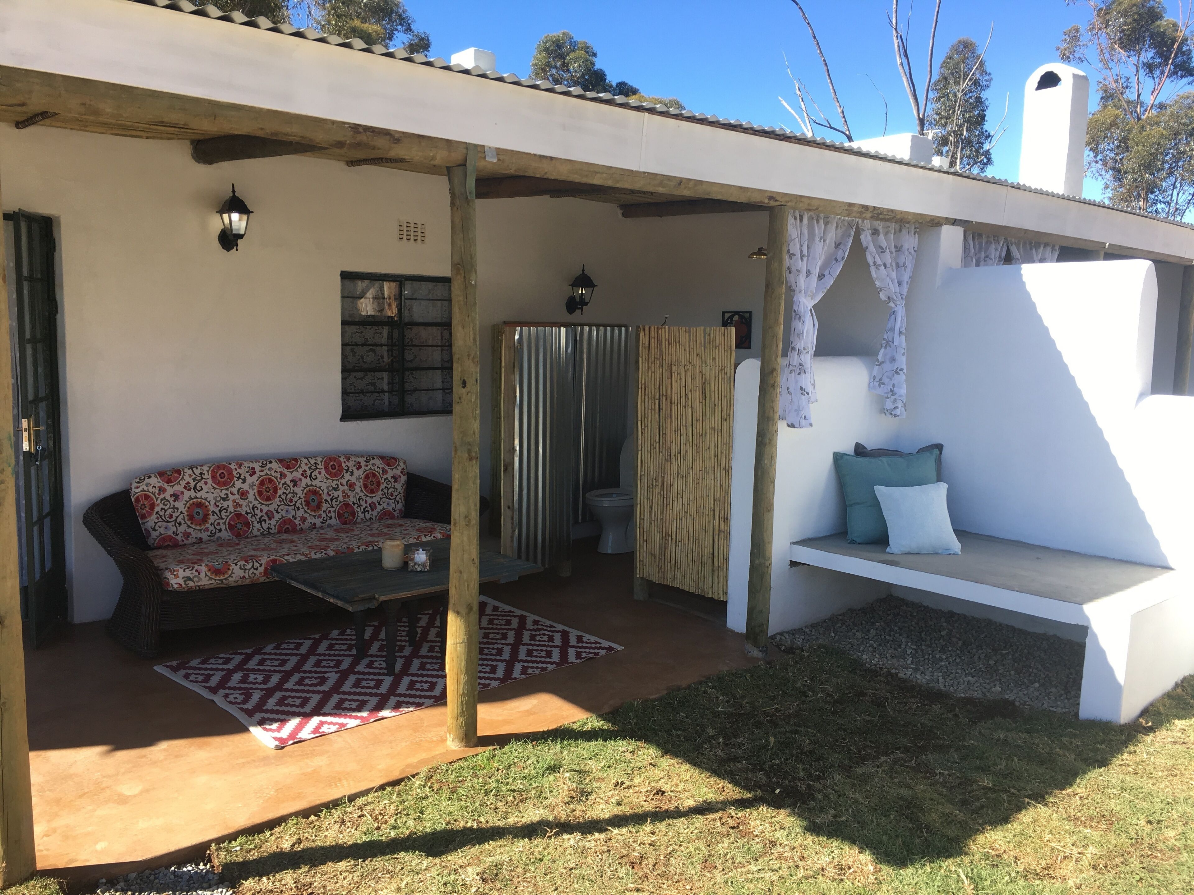 Uma área de estar coberta ao ar livre com um sofá e um banco, uma mesa pequena e um tapete estampado.