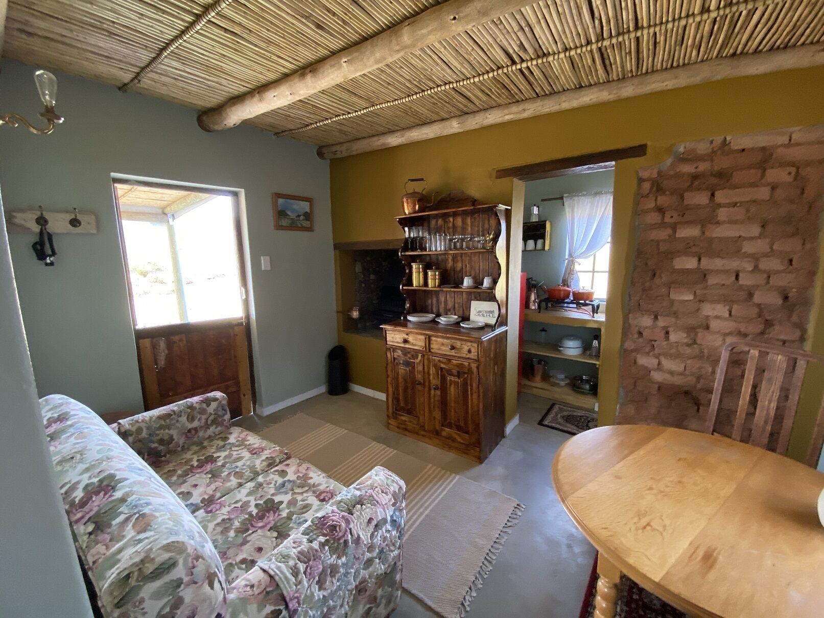 Un accogliente soggiorno con un divano floreale, un tavolo da pranzo in legno e un angolo cottura con mobili e scaffali in legno.
