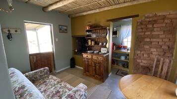Un accogliente soggiorno con un divano floreale, un tavolo da pranzo in legno e un angolo cottura con mobili e scaffali in legno.