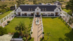 A large, white colonial-style building with a symmetrical facade, a central courtyard, and a well-maintained lawn. - Magic Hills - Ilanga Manor House (Ikwezi)